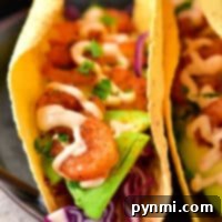 Close-up of two shrimp tacos with avocado slices, red cabbage, and creamy sauce in corn tortillas. Discover how to make shrimp tacos with frozen cooked shrimp for a quick and delightful meal option.