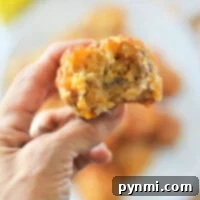 A hand holds a bitten savory Bisquick sausage balls, with a blurred background showcasing similar muffins on a plate.