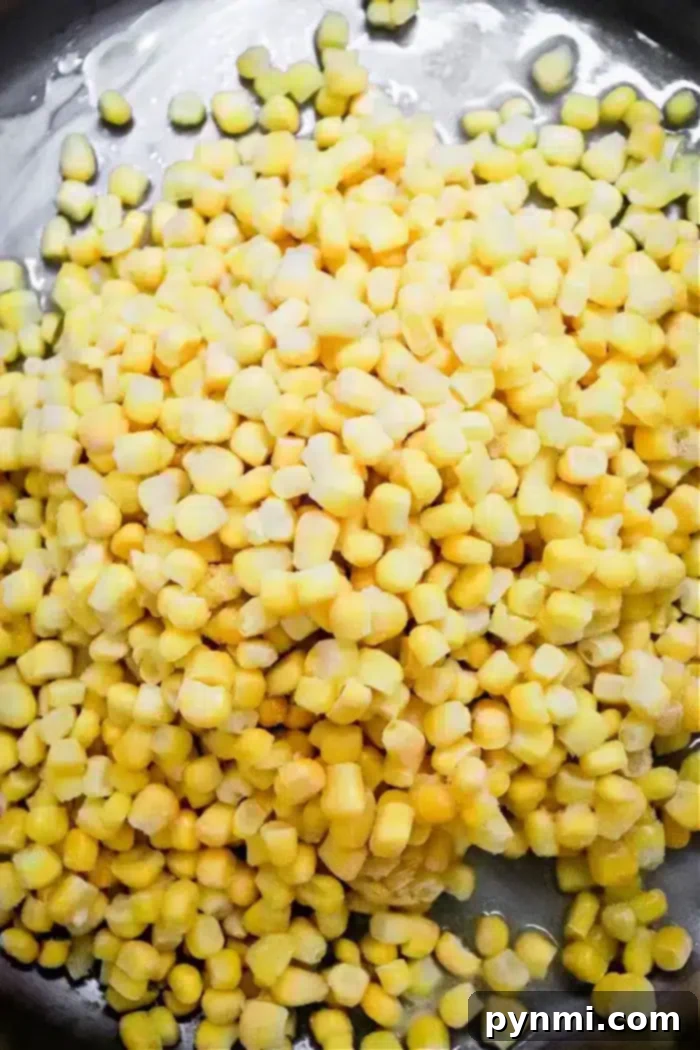 Golden Honey Butter Skillet Corn 3 A close-up view of a heap of fresh or possibly frozen yellow and white corn kernels, piled on a dark surface, promises the delicious potential of Honey Butter Skillet Corn.