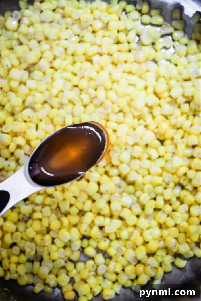 Golden Honey Butter Skillet Corn 5 A spoon with honey hovers above a skillet of Honey Butter Skillet Corn, perfectly sautéed for a deliciously sweet and savory dish.