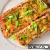 Plate with two slices of salmon topped with a rich mustard sauce and garnished with sliced green onions. A fork is on the side.
