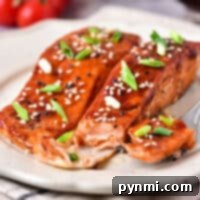 air fryer Teriyaki salmon fillets on a plate, topped with sesame seeds and green onions, surrounded by cherry tomatoes.