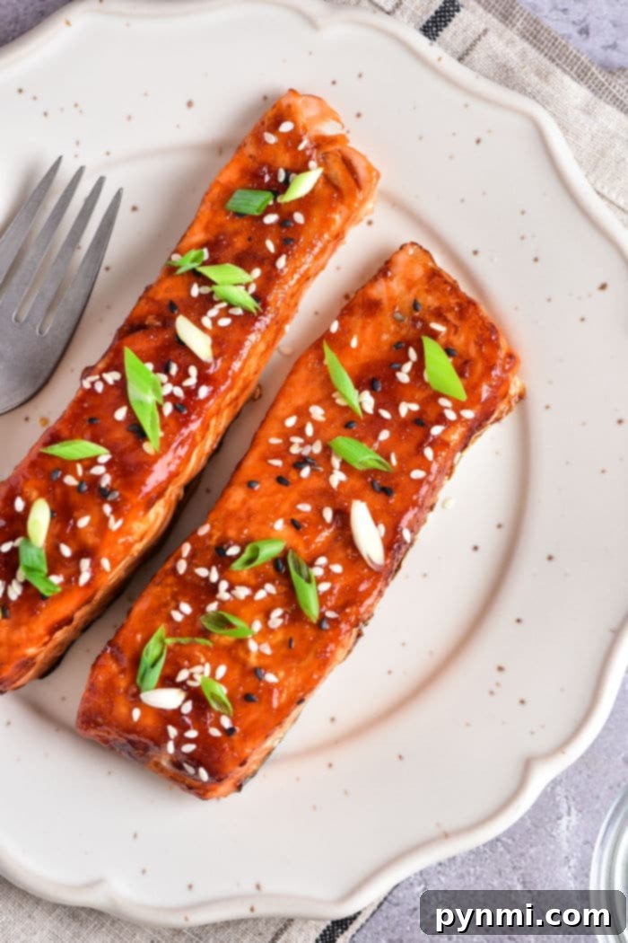 Teriyaki salmon air fried to perfection, sprinkled with sesame seeds and green onions, elegantly presented on a white plate alongside a fork.