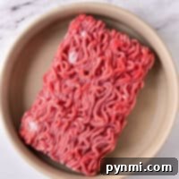 Frozen ground beef rests in a round beige dish on a a marble surface, ready for you to thaw ground beef in the microwave quickly and easily.