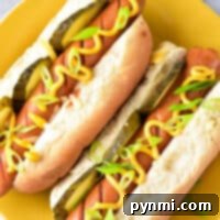 Two hot dogs with pickles, mustard, and green onions rest on a yellow plate. Want them quick? Here's a tip: learn how long to cook hot dogs in the microwave for perfectly heated bites.