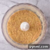Crafted Crumbs 6 Top view of a food processor bowl containing finely ground seasoned breadcrumbs on a gray marble surface.