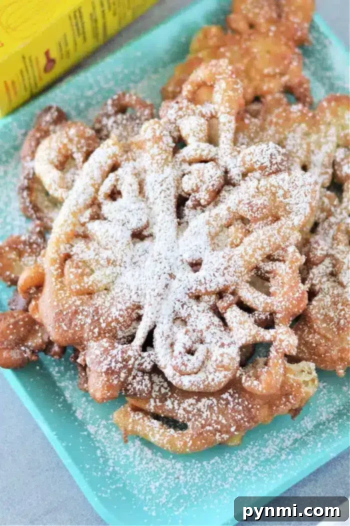 Bisquick Magic: 3-Ingredient Funnel Cakes 2 A plate of golden-brown Bisquick funnel cakes, generously dusted with powdered sugar, rests on a teal square dish. A yellow box of Bisquick is partially visible in the background, hinting at the simple ingredients used. The cakes display their characteristic intricate, swirling patterns.