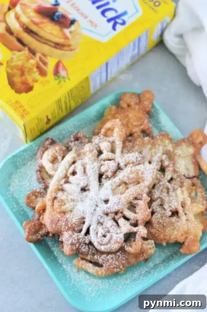 Bisquick Magic: 3-Ingredient Funnel Cakes 6 A plate with two freshly made Bisquick funnel cakes, generously dusted with powdered sugar, sits invitingly next to a yellow box of pancake mix. The cakes are golden brown and perfectly swirled.