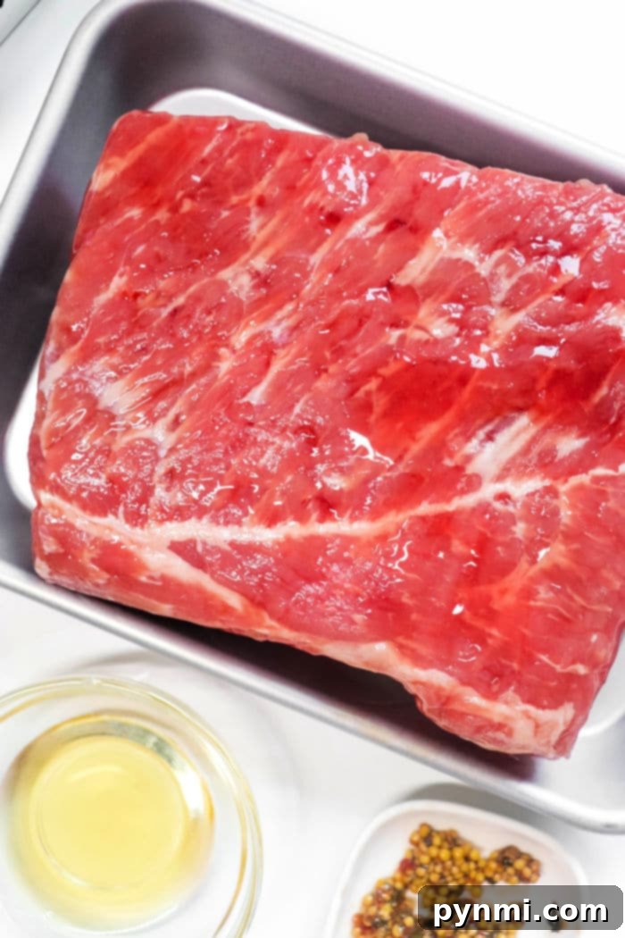 Air Fried Corned Beef Perfection 3 Raw corned beef brisket in a silver pan, ready to transform into delicious air fryer corned beef, sits next to a small bowl of oil and a dish of spices.