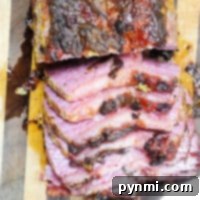 Air Fried Corned Beef Perfection 5 Sliced corned beef roast, reminiscent of air fryer corned beef, boasts a charred exterior on a wooden cutting board. The inside is pink with a glazed, crispy surface, and juices glisten on the board.