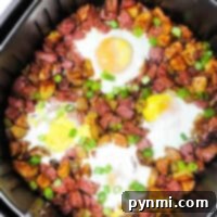 Crispy Air Fryer Corned Beef Hash 7 Air Fryer Corned Beef Hash breakfast with eggs, potatoes, and diced meat, topped with sliced green onions.
