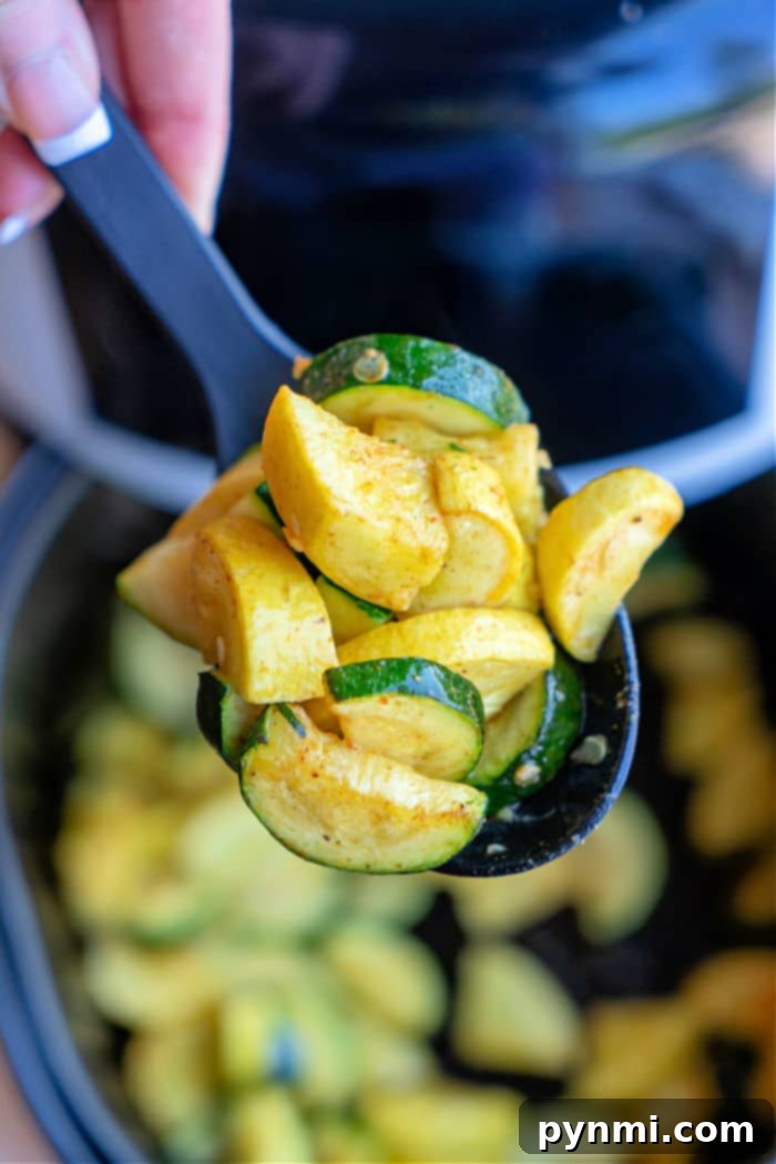 A spoon lifts air fried zucchini and squash slices, showcasing the vibrant colors of this air fryer squash and zucchini masterpiece above a pot.
