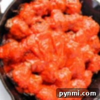 Learn how to cook meatballs on the stovetop with ease. Enjoy succulent meatballs, perfectly simmered in a bright red tomato sauce, all nestled in a rustic black cast iron skillet.