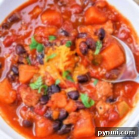 A bowl of Sweet Potato Chili with black beans, chunks of vegetables, cheese, all cooked to perfection in an Instant Pot and garnished with parsley.