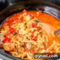 A slow cooker brimming with Mexican shredded chicken, tomatoes, and broth.