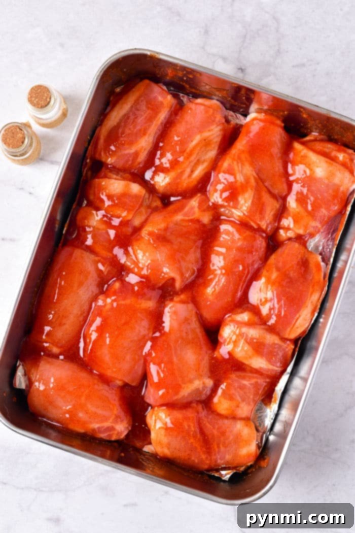How Long to Bake Chicken Wings at 375°F 5 Uncooked chicken wing pieces coated in vibrant red sauce, nestled in a baking tray, flanked by seasoning bottles. This image captures the delicious preparation phase for how long to cook chicken wings in oven at 375 degrees.