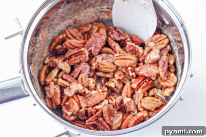How to Make Candied Pecans - A hand stirring pecans in a saucepan with sugar syrup.