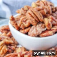A bowl brimming with stove-prepared candied pecans sits invitingly, while more pecans are playfully scattered on a striped cloth.