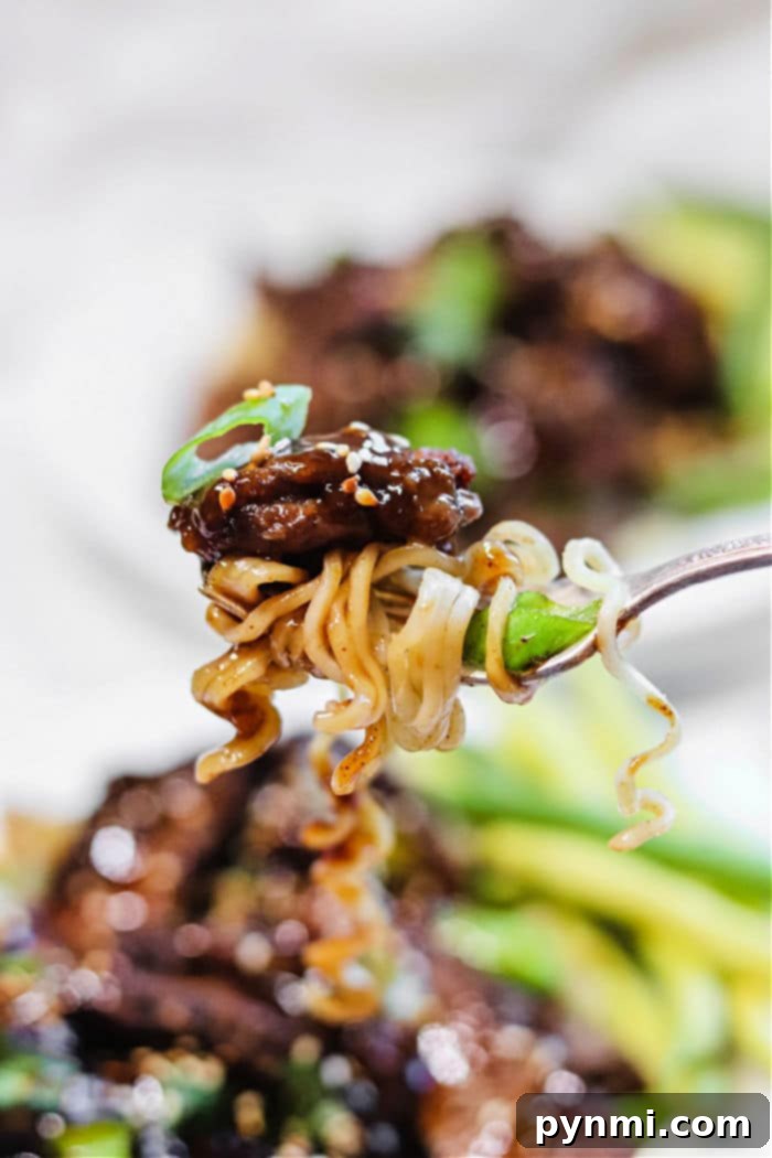 Close-up of a fork holding air fryer beef and noodles, sprinkled with sesame seeds and garnished with fresh green onions.