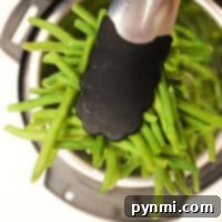 Tongs carefully hold green beans over an Instant Pot, illustrating how to cook frozen green beans effortlessly.