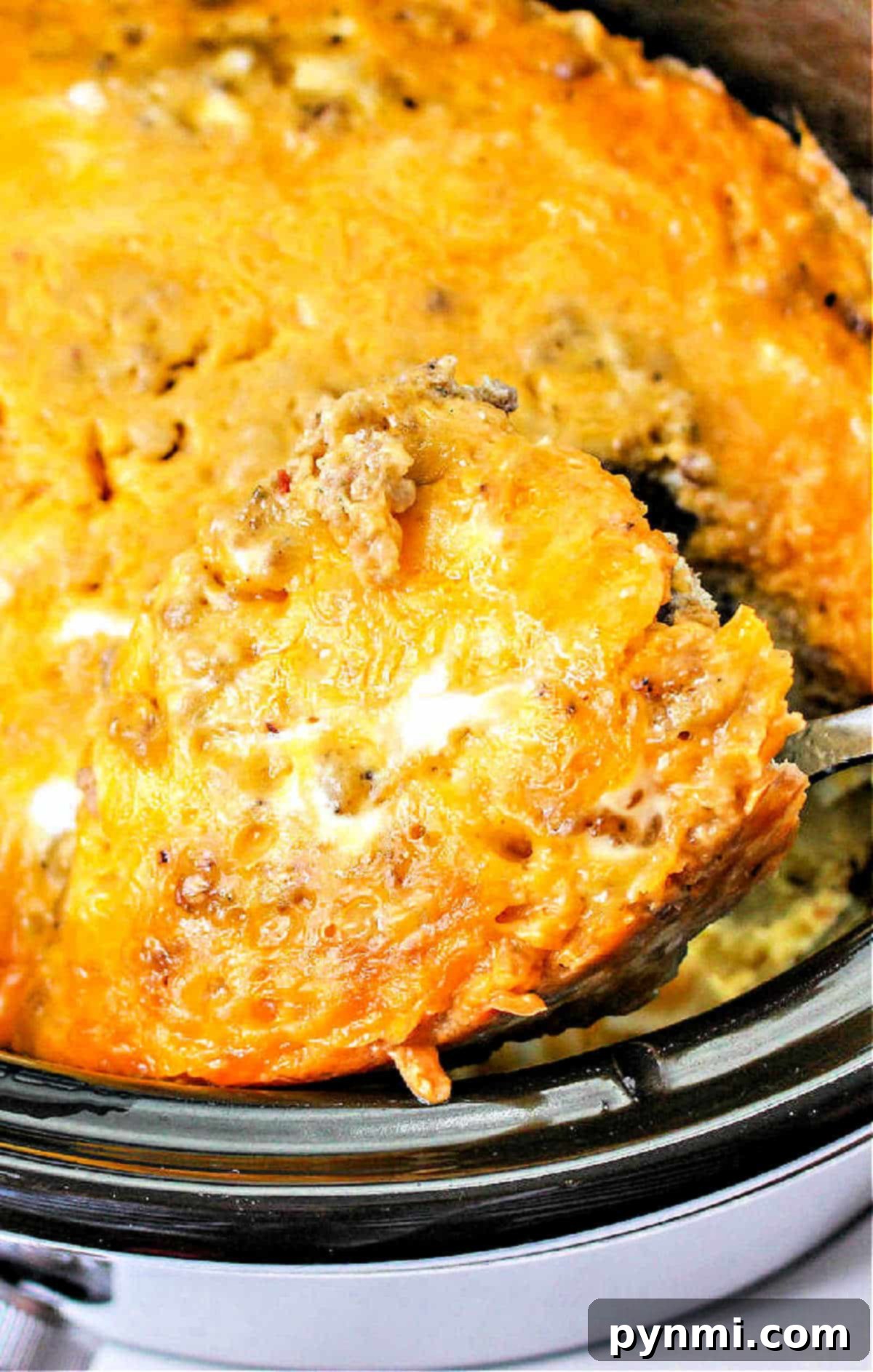 Effortless Slow Cooker Scramble 2 Serving spoon lifting a portion of fluffy, cheesy Crockpot scrambled eggs with visible pieces of sausage, evoking a comforting and delicious breakfast.