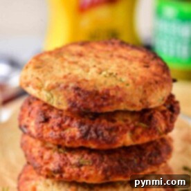 Stack of four golden brown ground turkey patties on parchment paper, with condiments blurred in the background.