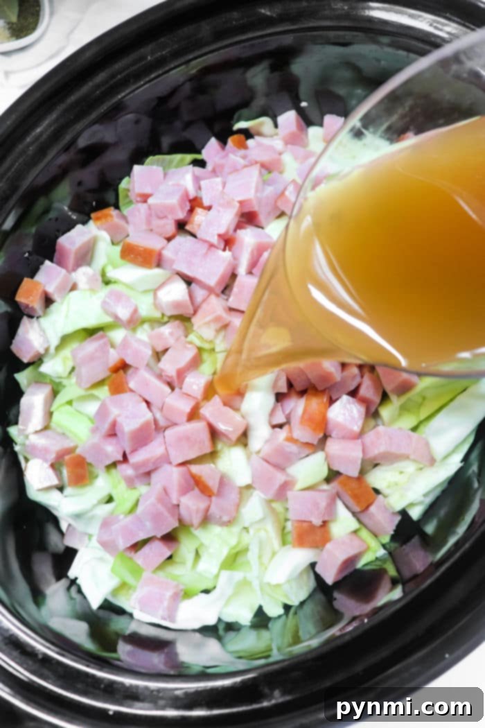 A close-up shot of slow cooker cabbage and ham, with butter pats melting on top, indicating the start of a comforting cooking process.