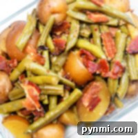 Glass dish featuring vibrant green beans with ham and tender small potatoes, sprinkled with crispy bacon pieces.