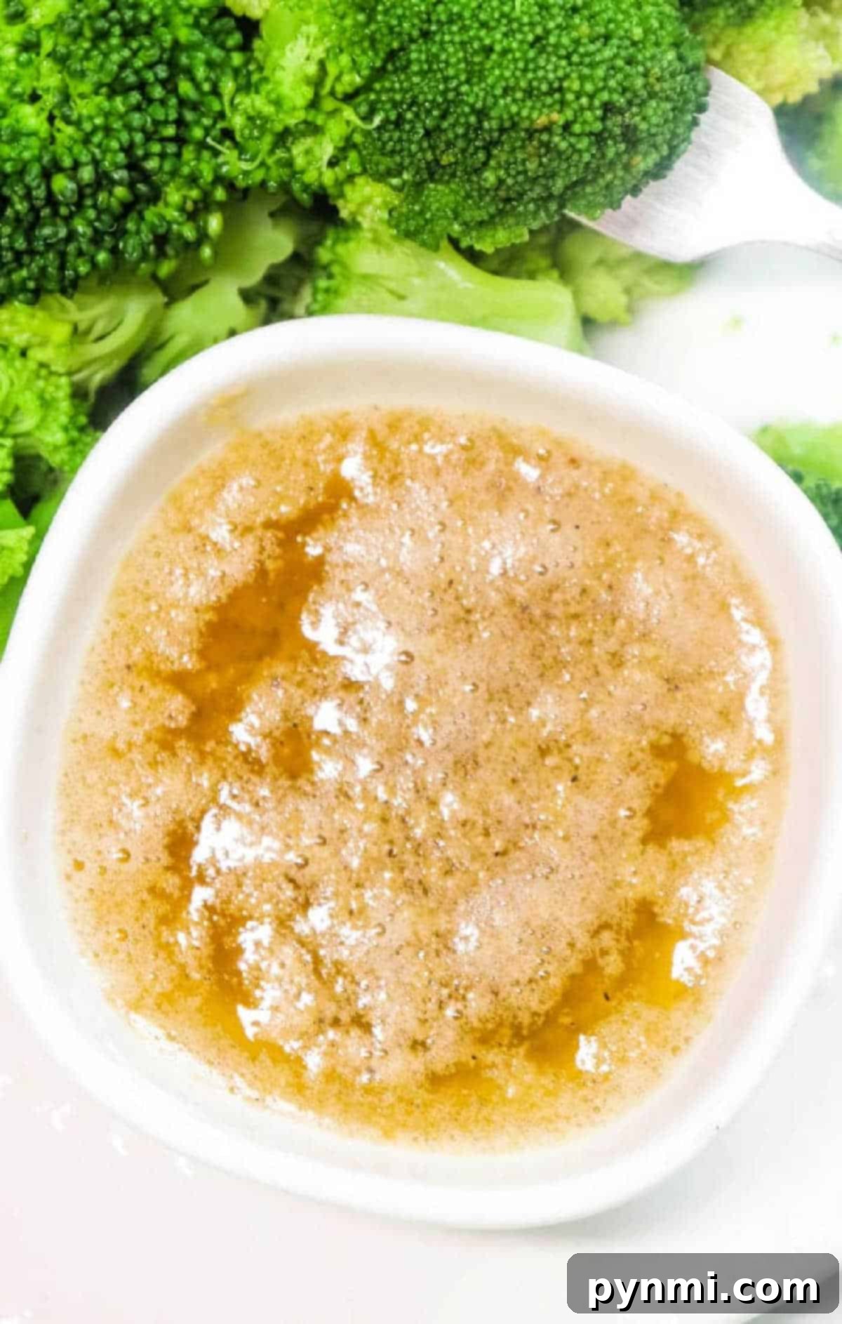 A bowl of Cajun Garlic Butter Sauce next to steamed broccoli florets with a fork.