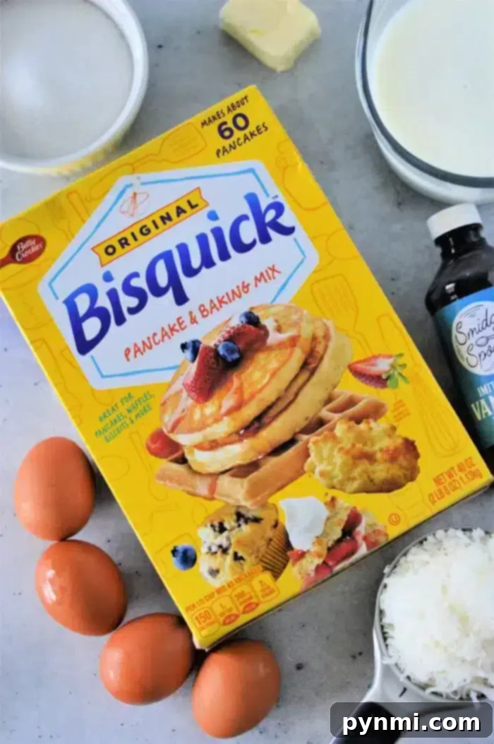 Magic Coconut Bisquick Pie 3 A box of Bisquick pancake and baking mix sits on a gray surface, ready for use in the Bisquick Impossible Coconut Pie Recipe. It is surrounded by essential ingredients: three fresh eggs, a bowl of creamy milk, a stick of butter, a bottle of vanilla extract, and a cup of delicate shredded coconut.