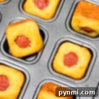 Mini corndog muffins, also known as Corn Dog Bites, nestle in a baking tray, each with a small hot dog snugly in the center.