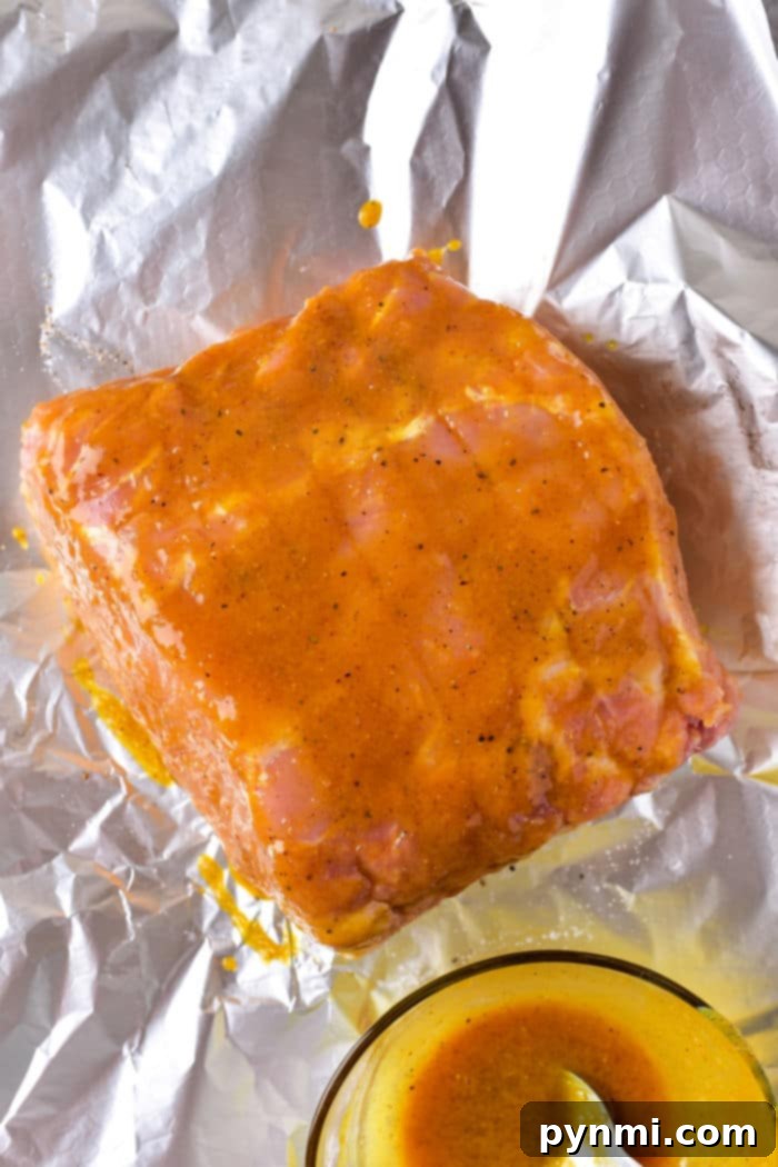 Raw pork roast coated in a bright mustard marinade sits on aluminum foil, with a bowl of the marinade beside it, ready to be transformed just like learning how long to cook a pork roast in the oven at 375 degrees