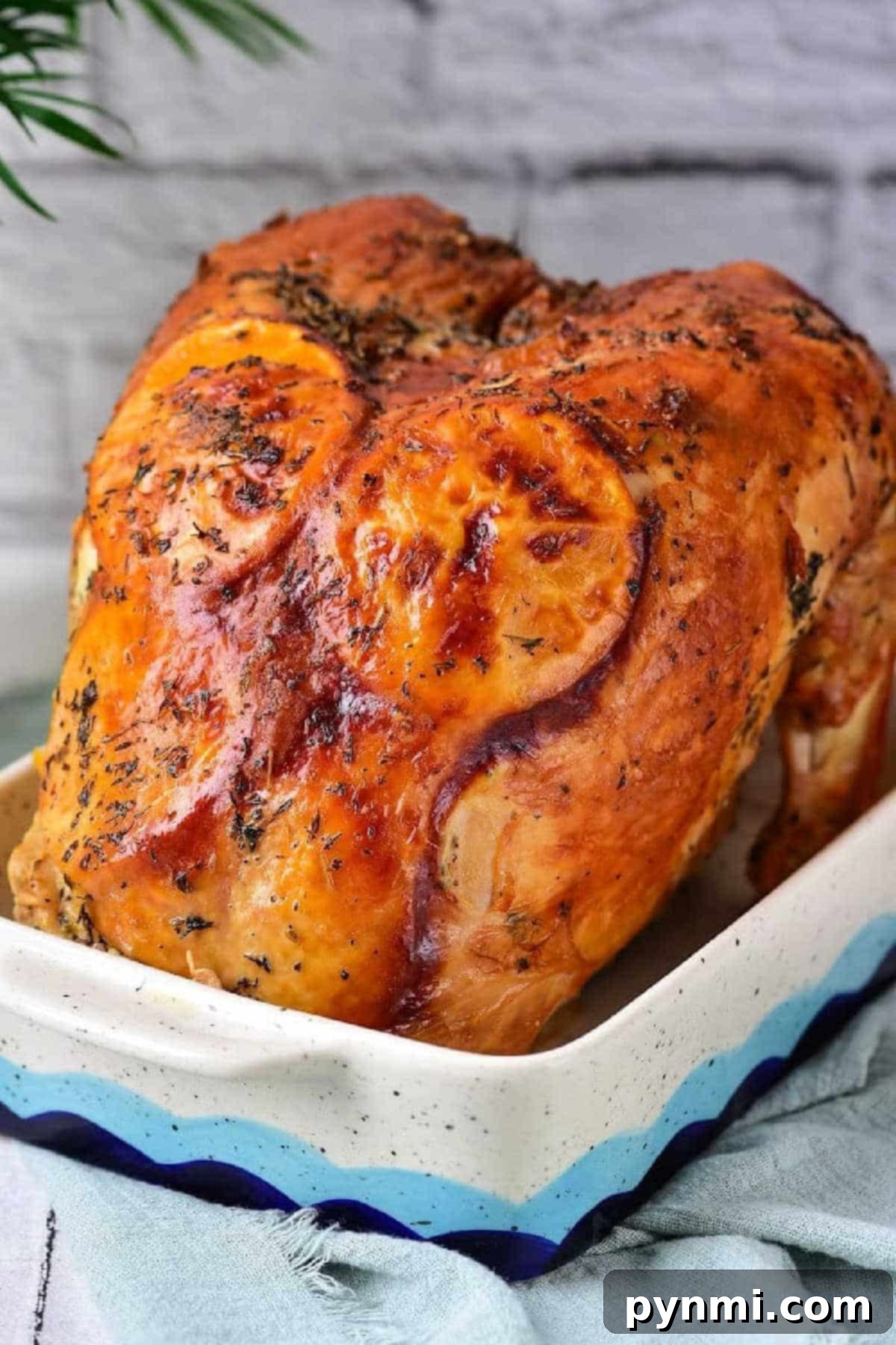 Golden Roasted Turkey Crown 2 Golden roasted Turkey Crown breast with herbs in a rectangular ceramic dish, against a light brick background.