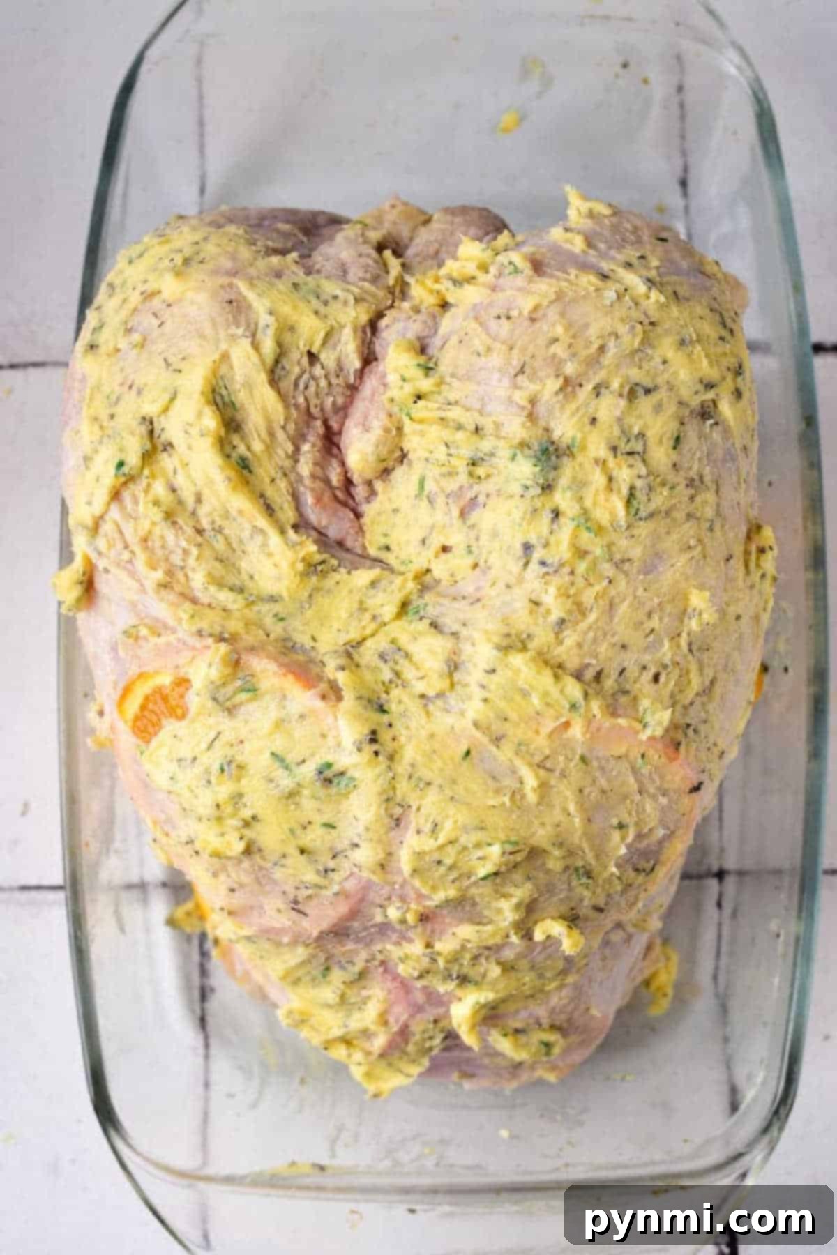 Golden Roasted Turkey Crown 5 Raw Turkey Crown coated with a yellow herb butter mixture in a glass baking dish.