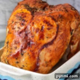 A deliciously roasted turkey crown with fragrant herbs graces a white baking dish, perfectly complemented by the rustic charm of a brick backdrop.