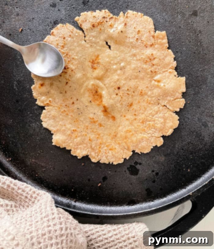 Mastering Roti at Home 5 Roti cooking on a skillet with a spoon, next to a textured cloth, offers a snapshot of how to make roti perfectly at home.