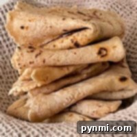 Mastering Roti at Home 7 A stack of folded flatbreads, reminiscent of those made in traditional roti recipes, rests elegantly on a textured, light brown cloth.