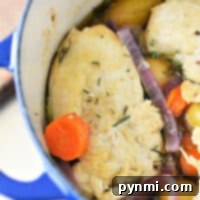 A blue Dutch oven brimming with tender chicken breast, carrots, potatoes, and red onions in a savory broth, all garnished with fragrant rosemary.