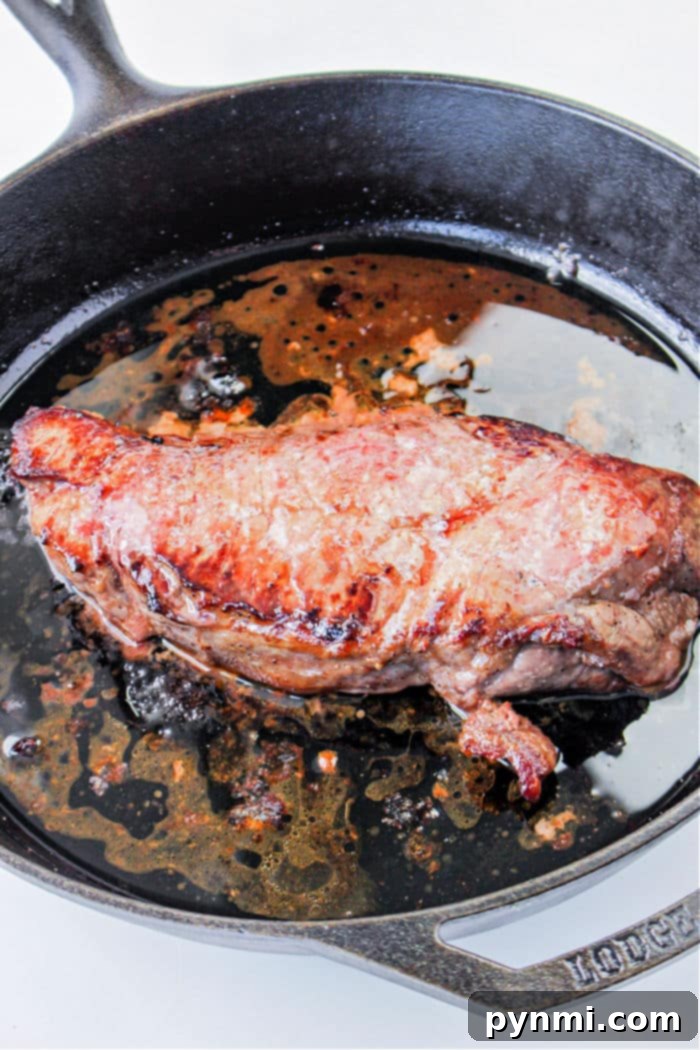 Cast Iron Seared Flank Steak 4 A juicy flank steak sizzling intensely in a hot cast iron skillet, capturing the perfect sear against a simple white background.