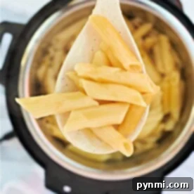 A wooden spoon holds perfectly cooked penne pasta, lifted gracefully above a pot. This delightful sight brings to mind the convenience and efficiency of preparing meals like pressure cooker pasta, where flavors meld seamlessly and every bite promises savory satisfaction.