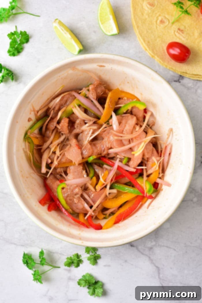 Sizzling Chicken Fajita Wraps 3 A bowl of marinated chicken with sliced bell peppers and onions, reminiscent of chicken fajita tacos, is surrounded by lime wedges and parsley for a vibrant presentation.