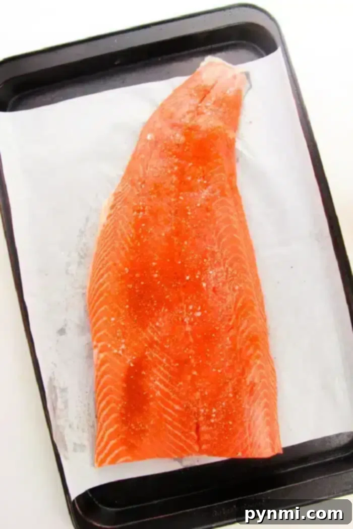 A pristine raw salmon fillet, seasoned and ready for the oven, resting on parchment paper on a baking sheet. It's the perfect preparation for baking salmon at 400 degrees to ensure even cooking.