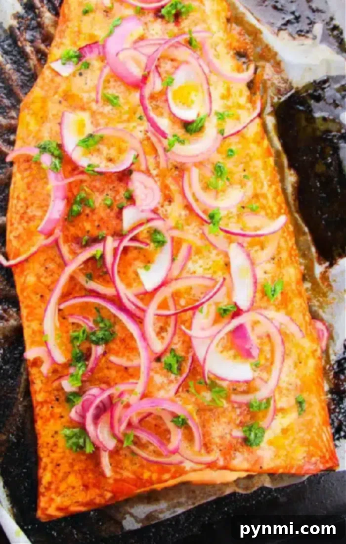 A perfectly cooked fillet of salmon on a baking tray, adorned with thinly sliced red onions and garnished with chopped green herbs, showcasing its flaky texture.
