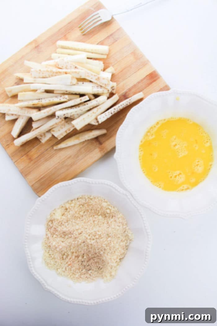 Golden Crispy Air Fryer Eggplant 3 Eggplant sticks on a cutting board sit patiently beside bowls of beaten eggs and breadcrumbs, eager to become the perfect companions to crispy eggplant fries.
