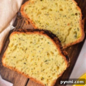 Two slices of zucchini lemon poppy seed bread rest on a wooden board with a lemon wedge nearby.