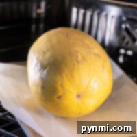 A whole yellow spaghetti squash is roasting to perfection on parchment paper, nestled in the warmth of the oven.