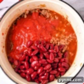 A Dutch oven on the stovetop brims with a hearty chili made from kidney beans, ground meat, and tomatoes.