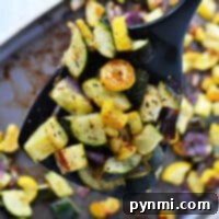 A spoonful of perfectly roasted zucchini and squash, accompanied by tender onions, adorns the baking tray.
