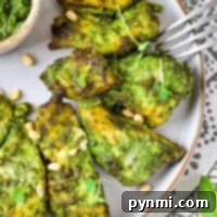 Air Fryer Pesto Chicken pieces are perfectly grilled and coated in green pesto sauce, served on a plate garnished with fresh greens and pine nuts.