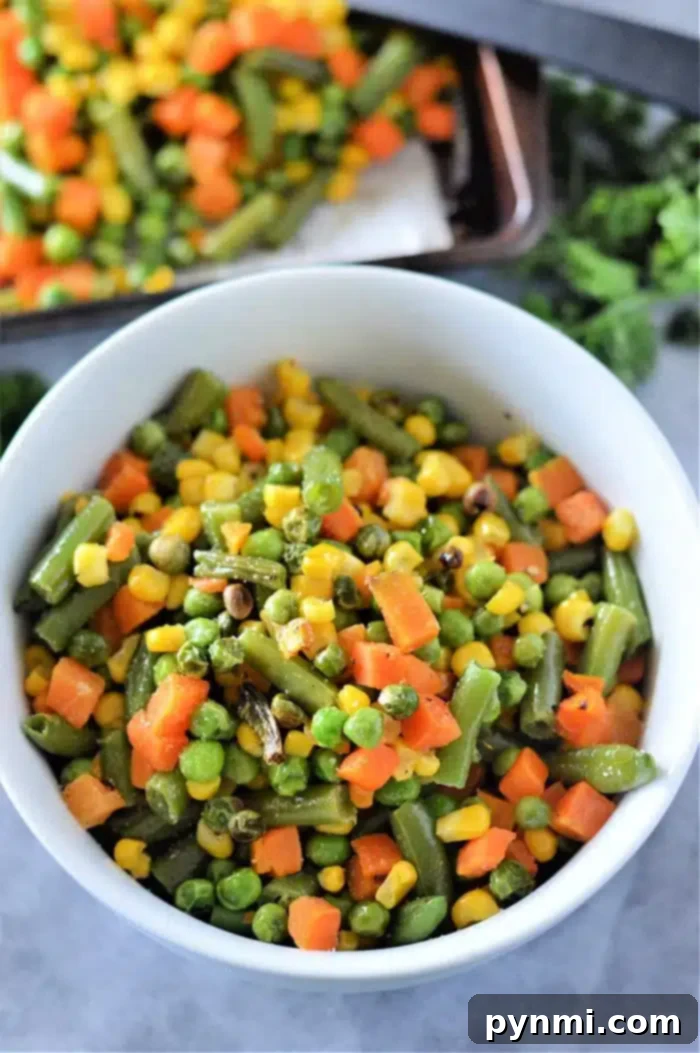 Frozen to Fantastic: Roasting Your Veggies 2 A bowl filled with perfectly roasted mixed vegetables, including vibrant green beans, golden corn, tender peas, and diced carrots. The crisp texture and rich colors suggest they were expertly cooked from frozen, ready to be served. In the background, a baking tray holds more vegetables, implying a larger batch was prepared.